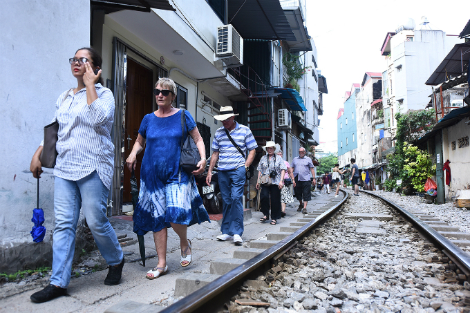 Tourists walk the narrow lane between the rail line and houses.